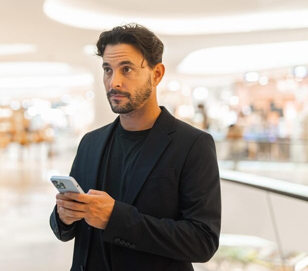 portrait-happy-handsome-hispanic-businessman-using-phone-window-shopping-mall_251136-89049